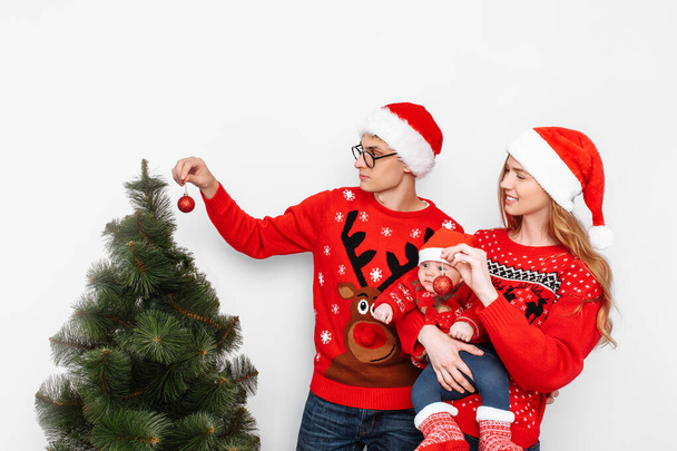 Happy family in Christmas hats, mom dad and little child celebrate Christmas and decorate the Christmas tree. - Foto, Imagen