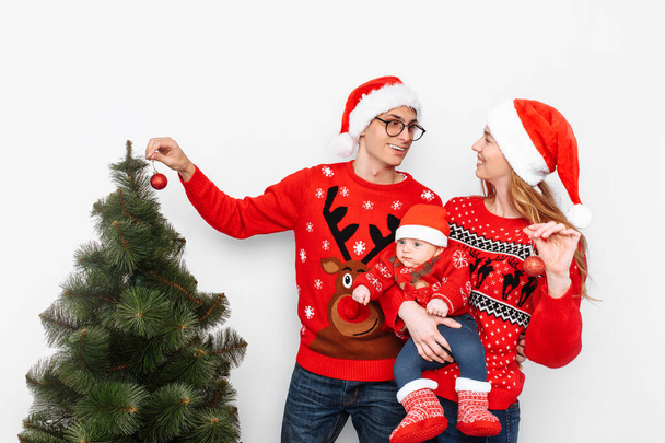 Happy family in Christmas hats, mom dad and little child celebrate Christmas and decorate the Christmas tree. - Fotoğraf, Görsel