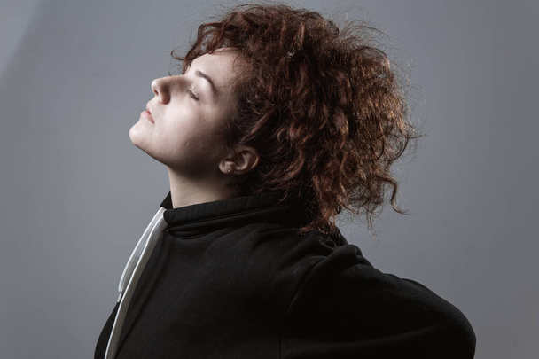 Portrait of a beautiful curly-haired girl with redheads on a gray background - Fotó, kép
