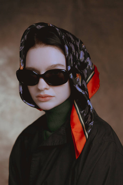 Elegantes grandes retratos de una chica en gafas y una bufanda en un estudio sobre un fondo de lona
 - Foto, Imagen