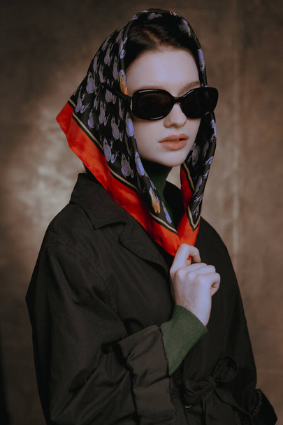 Κομψή μεγάλα πορτρέτα ενός κοριτσιού με γυαλιά και ένα μαντήλι σε ένα στούντιο σε φόντο καμβά - Φωτογραφία, εικόνα