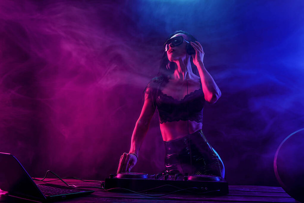 Young sexy woman dj playing music. Headphones and dj mixer on table. - Фото, изображение