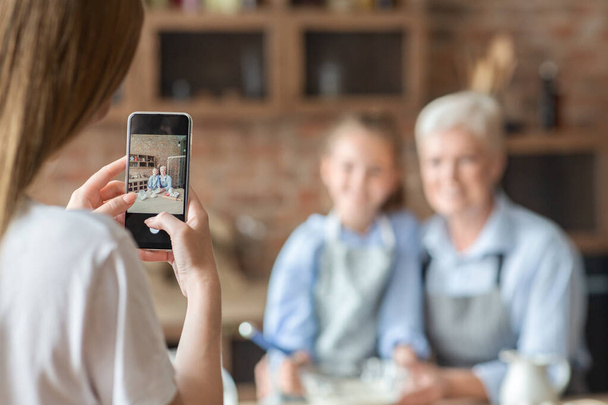 Woman taking photo on smartphone in kitchen - Zdjęcie, obraz