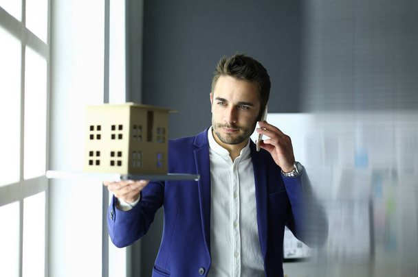 Businessman holding house miniature on hand standing in office. - Photo, image