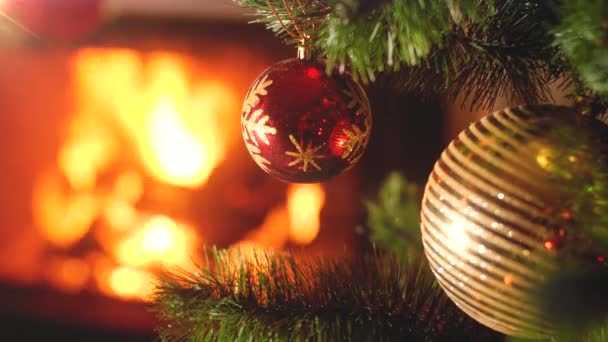 Closeup vídeo 4k de bugigangas vermelhas e douradas penduradas na árvore de Natal contra o fogo ardente em firepalce na casa. Belo cenário para férias de inverno
 - Filmagem, Vídeo