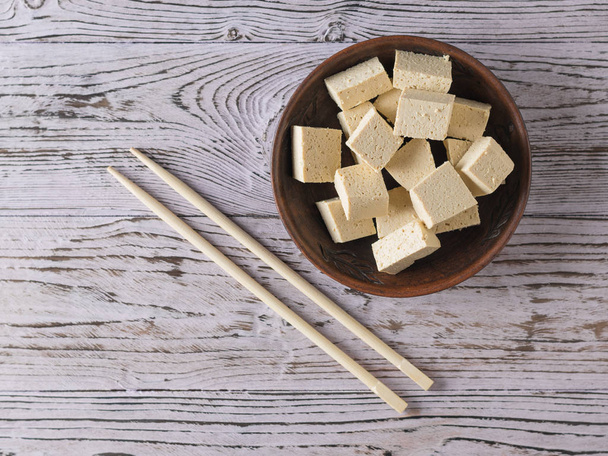 Hůlky a kousky tofu sýra v hliněné misce na dřevěném stole. Sójový sýr. Plocha. - Fotografie, Obrázek