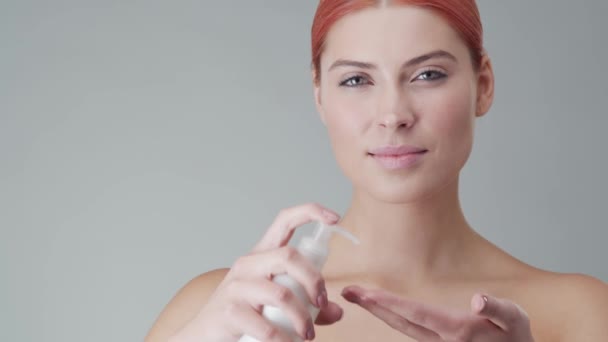 Studio portrait of young, beautiful and natural redhead woman applying skin care cream. Face lifting, cosmetics and make-up. - Séquence, vidéo