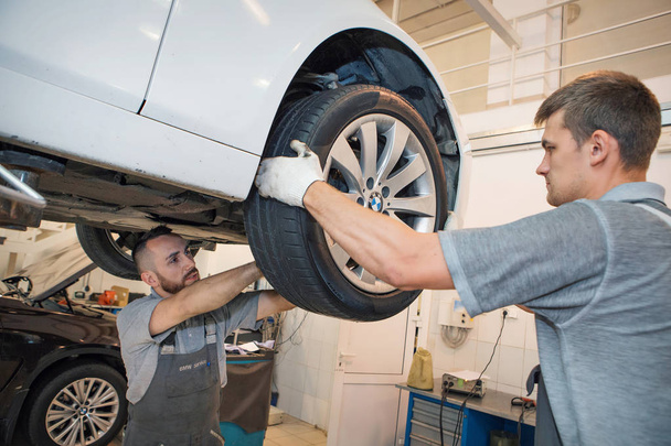 car repair, BMW advertising, Moscow, 1.11.2018: car repair: wheel replacement closeup. mechanic screwing or unscrewing car wheel at car service garage - Фото, изображение