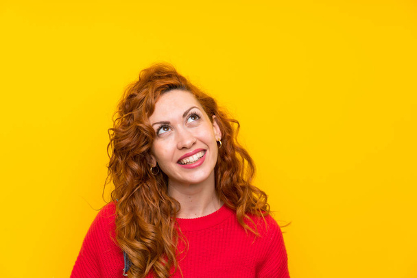 Femme rousse avec salopettes sur mur jaune isolé riant et levant les yeux
 - Photo, image