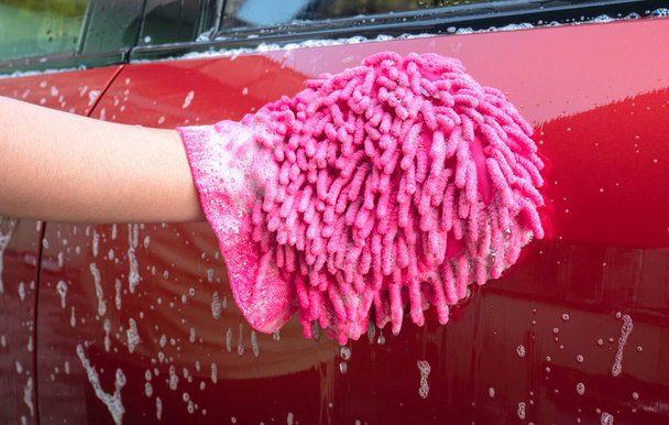 Main féminine tenant gant rose avec bulles pour laver la voiture
. - Photo, image