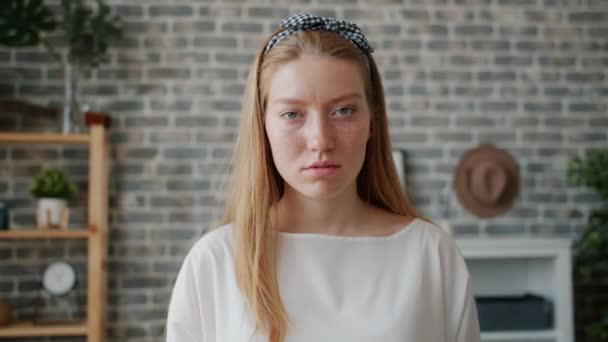 Slow motion portrait of young woman with serious face looking at camera indoors - Filmati, video