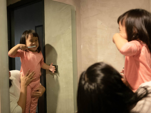 Очаровательная азиатская девочка чистит зубы перед зеркалом
 - Фото, изображение