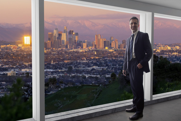 オフィスの窓からロサンゼルスのダウンタウンの建物を見てスーツを着たビジネスマン。ラで働いている建築家や不動産開発業者のような政治家に見えます. - 写真・画像