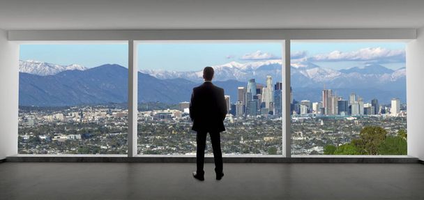 ロサンゼルスのダウンタウンの景色を眺めるオフィスのビジネスマン。男はカリフォルニアで働いている上司や地域マネージャーのように見えます.背景は冬の雪のサンガブリエル山脈を示しています.  - 写真・画像
