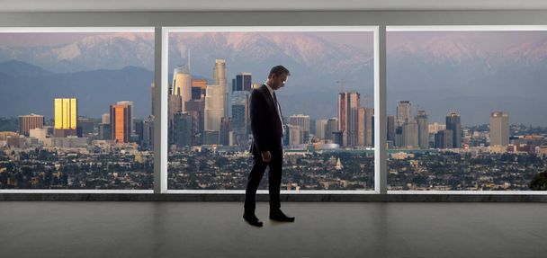 Geschäftsmann in einem Büro mit Blick auf die Innenstadt von Los Angeles. der mann sieht aus wie ein boss oder ein regionalmanager, der in kalifornien arbeitet. der hintergrund zeigt die schneebedeckten san gabriel berge im winter.  - Foto, Bild