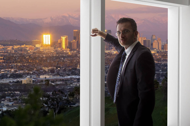 Liikemies puvussa katselee Los Angelesin keskustan rakennuksia toimiston ikkunasta. Hän näyttää poliitikolta, pormestarilta, arkkitehdiltä tai kiinteistökehittäjältä, joka työskentelee LA:ssa.
. - Valokuva, kuva