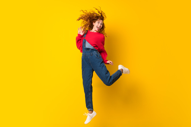Punapää nainen haalarit hyppäämällä yli eristetty keltainen seinä
 - Valokuva, kuva