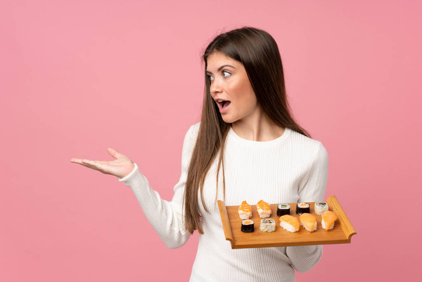 Young girl with sushi over isolated pink background with surprise facial expression - 写真・画像
