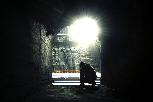 A man in a dark underground corridor in blur. Blurry image of a squatting man in an underground corridor - Photo, Image