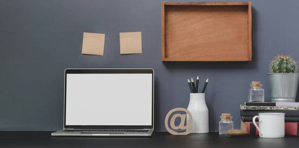 Open blank screen laptop computer in modern workspace with decorations and office supplies on black desk and grey wall  - 写真・画像