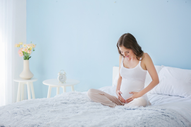 美しい妊娠中の女性座っていますベッドに家 - 写真・画像