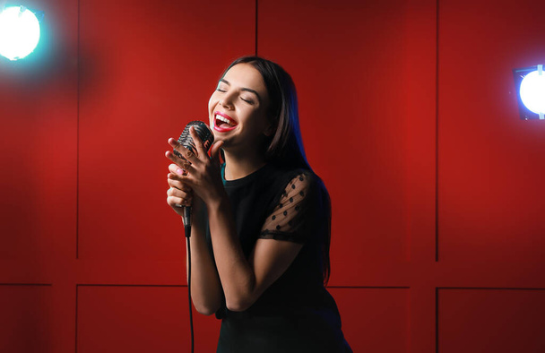 Krásná mladá zpěvačka s mikrofonem na barevném pozadí - Fotografie, Obrázek