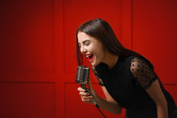 Όμορφη νεαρή τραγουδίστρια με μικρόφωνο στο φόντο χρώμα - Φωτογραφία, εικόνα