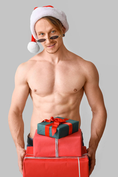 Молодий спортсмен Санта Клаус з дарами на сірому фоні. - Фото, зображення
