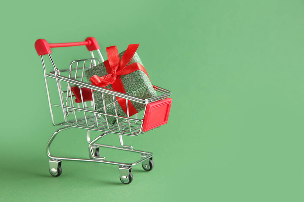 Small shopping cart with gift on color background - Photo, Image