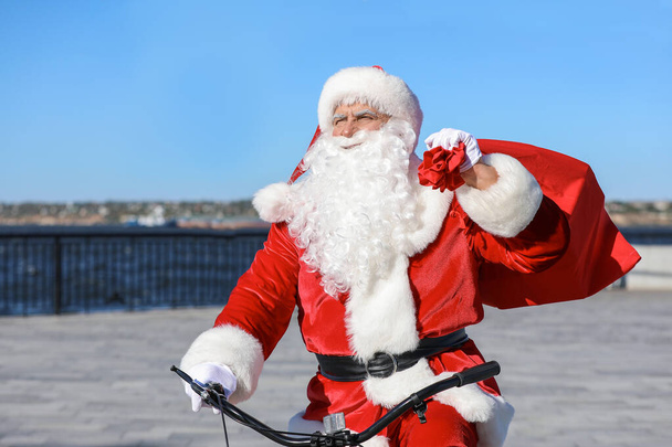 Санта-Клаус с сумкой на велосипеде на открытом воздухе
 - Фото, изображение