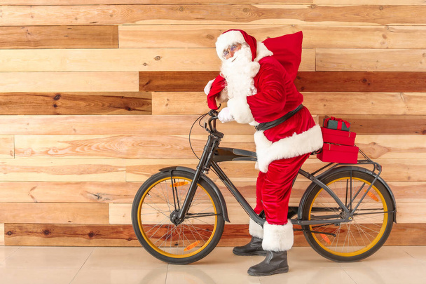 Санта-Клаус с рождественскими подарками и велосипедом возле деревянной стены
 - Фото, изображение