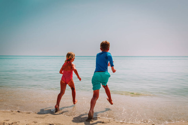 Ευτυχισμένο αγόρι και κορίτσι τρέχουν να κολυμπήσουν στην παραλία - Φωτογραφία, εικόνα