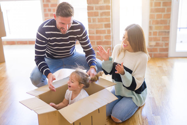 Όμορφη οικογένεια, παιδί που παίζει με τους γονείς του ιππασία χάρτινο κουτί στο νέο σπίτι - Φωτογραφία, εικόνα