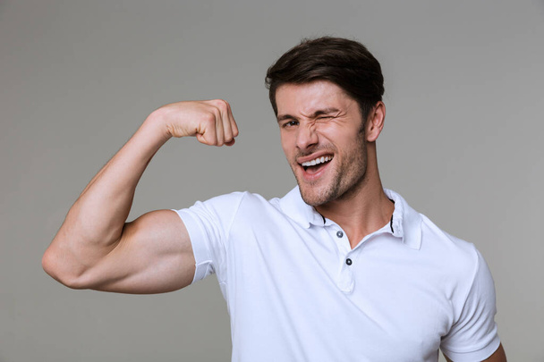 Obrázek bělošského bruneta muže s úsměvem a ukazující jeho biceps - Fotografie, Obrázek