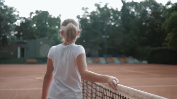 sports hobby, professional teen girl tennis player with racket touches tennis net and walks along court after championship under rain - Πλάνα, βίντεο