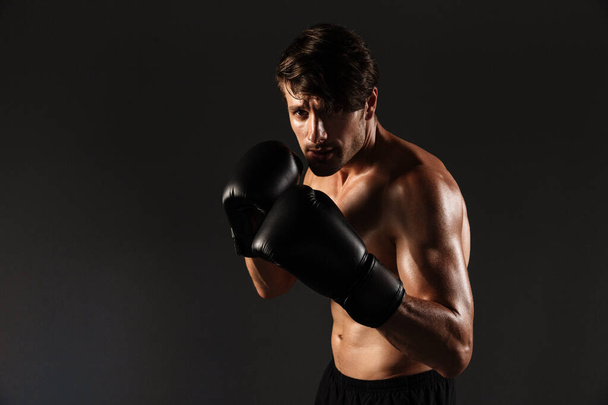 Handsome young strong sportsman boxer in gloves make exercises boxing isolated over black wall background. - Фото, зображення