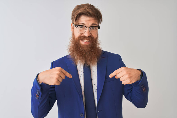 Young redhead irish businessman wearing suit and glasses over isolated white background looking confident with smile on face, pointing oneself with fingers proud and happy. - Photo, Image