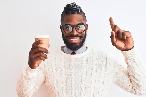 Afro-Amerikaanse man met vlechten drinken af te nemen koffie over geïsoleerde witte achtergrond verrast met een idee of vraag wijzend vinger met gelukkig gezicht, nummer een - Foto, afbeelding