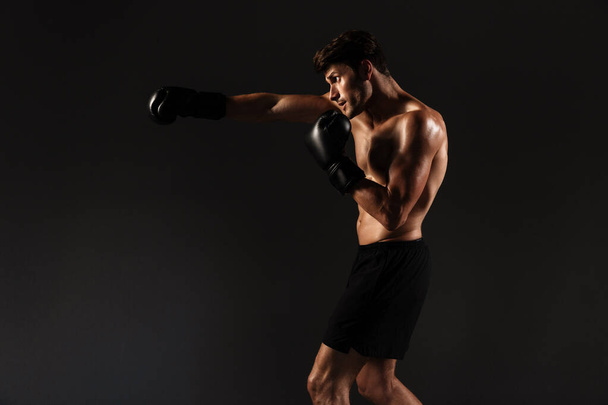Przystojny młody silny bokser sportowy w rękawiczkach sprawia, że ćwiczenia boks izolowane na tle czarnej ściany. - Zdjęcie, obraz