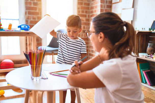 Krásná učitelka a batole chlapec kreslení čerpat pomocí barevných tužek ve školce - Fotografie, Obrázek