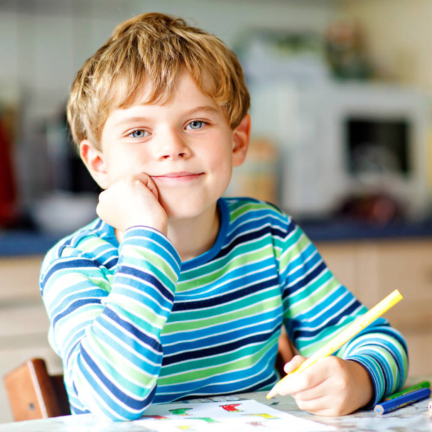 Porträt eines süßen gesunden, glücklichen Schuljungen, der zu Hause Hausaufgaben macht. Kleines Kind schreibt mit Buntstiften, drinnen. Grundschule und Bildung. Kind lernt Buchstaben und Zahlen schreiben - Foto, Bild