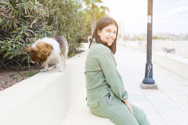 jonge mooie vrouw zitten op bank in de prominade met haar hond - Foto, afbeelding