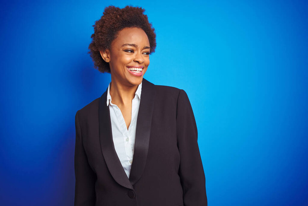 Afro-amerikai üzleti végrehajtó nő több mint elszigetelt kék háttér látszó el oldalra mosolyogva az arcon, a természetes kifejezés. Nevetve magabiztos. - Fotó, kép