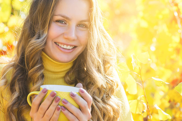Closeup portrét mladé krásné ženy na podzimním pozadí. Stylová atraktivní žena v době pádu. Blondýnka se kudrnatými vlasy na pití kávy. - Fotografie, Obrázek