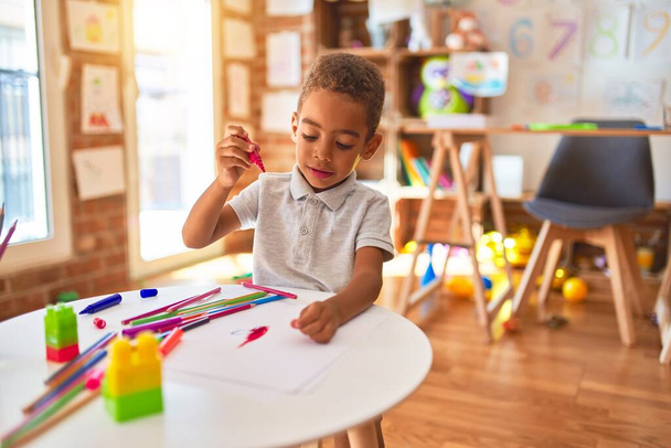 Beau dessin de bambin afro-américain en utilisant du papier et un stylo marqueur souriant à la maternelle
 - Photo, image