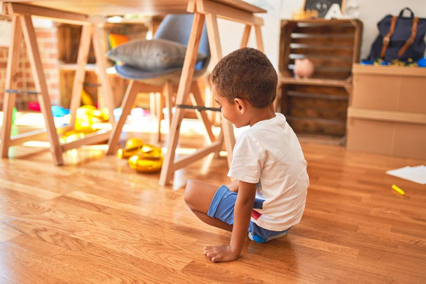 Beau bambin afro-américain assis sur le sol et souriant autour de beaucoup de jouets à la maternelle
 - Photo, image