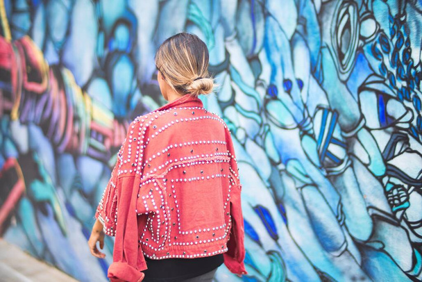 Nuori kaunis tyttö yllään punainen takki seisoo taaksepäin yli värikäs seinä kaupungin kadulla
 - Valokuva, kuva