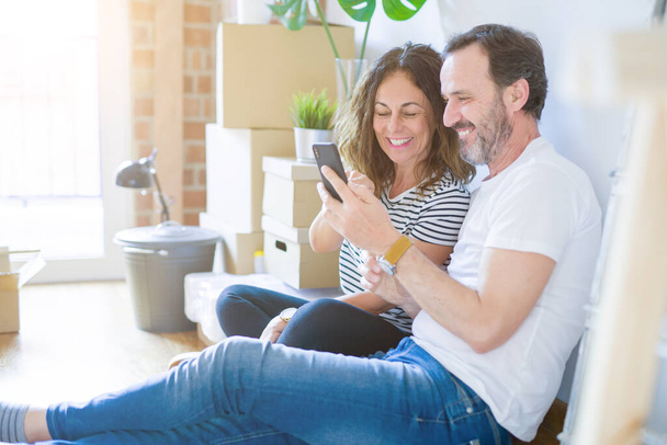 Középkorú Senior romantikus pár szerelmes ül a lakásban padló dobozok körül, és segítségével smartphone mosolygó boldog költöznek új otthont - Fotó, kép
