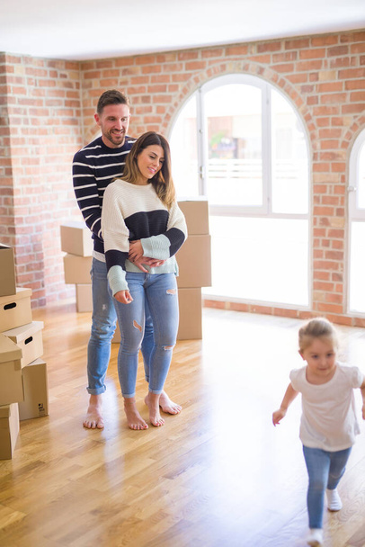 Beautiful family with a kid standing at new home around cardboard boxes - Foto, afbeelding