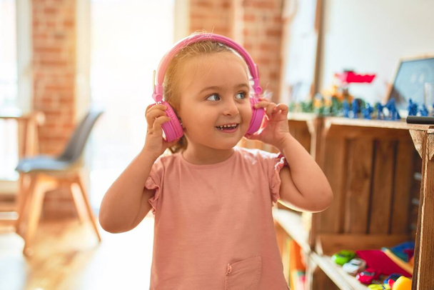 Gyönyörű szőke kisbaba lány zenét hallgat fejhallgatóval az óvodában - Fotó, kép